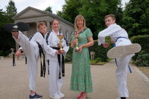 Two males doing a Taekwondo kick and two females holding a trophy.
