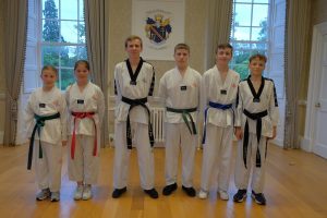 Five males and females standing indoors in Taekwondo clothing.