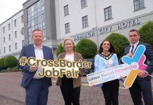 Four individuals standing in front of the Armagh City Hotel holding signs related to the "#CrossBorderJobFair Labour Market Partnership Working Together" event.