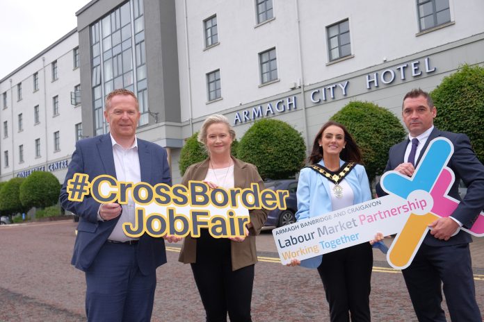 Four individuals standing in front of the Armagh City Hotel holding signs related to the 