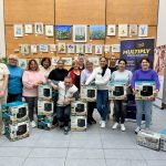 A group of people standing wth boxes containing air fryers and slow cookers, with a banner for Multiply