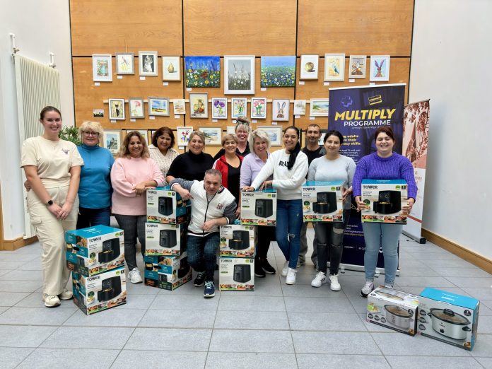 A group of people standing wth boxes containing air fryers and slow cookers, with a banner for Multiply