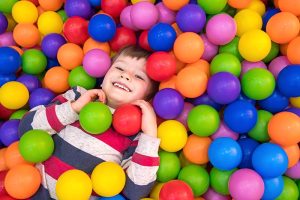 A child in lying in a soft play area surrounded by colourful small balls.