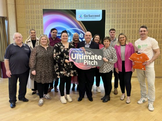 A group of men and women holding a sign for The Ultimate Pitch in front of a backdrop for Go Succeed Business Support