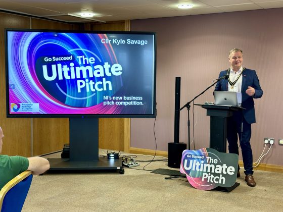 Deputy Lord Mayor presenting at a lectern with a sign for The Ultimate Pitch on a large tv screen