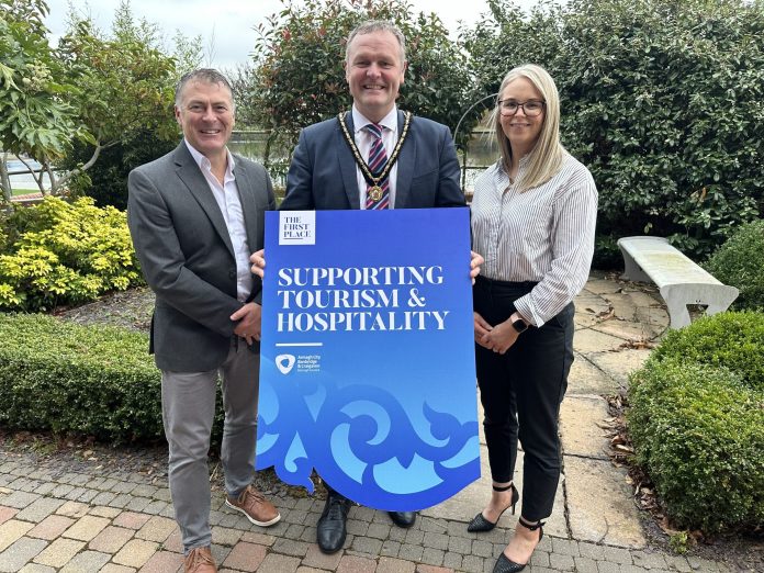 Three adults - two males and one female are holding a prop to promote the ABC Council's Sustainable Business Programme for tourism businesses.