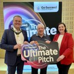 Three people holding a sign that says Ultimate Pitch, with a backdrop for Go Succeed Business Support