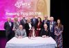 A group of dignitaries standing with a table in front and signs for Mid South West on a screen behind them.