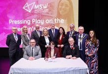 A group of dignitaries standing with a table in front and signs for Mid South West on a screen behind them.