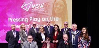 A group of dignitaries standing with a table in front and signs for Mid South West on a screen behind them.