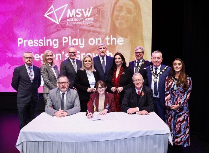 A group of dignitaries standing with a table in front and signs for Mid South West on a screen behind them.