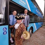 Three people standing at the entrance door of a Translink bus. One person is dressed as a living history character.