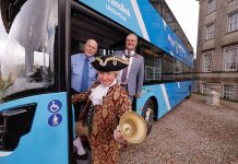 Three people standing at the entrance door of a Translink bus. One person is dressed as a living history character.