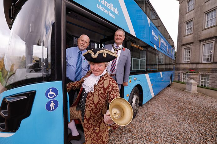 Three people standing at the entrance door of a Translink bus. One person is dressed as a living history character.