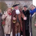 A group of people standing beside a man dressed in Georgian clothes.