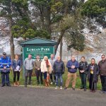 A number of people standing in a line in front of a sign that says Lurgan Park.