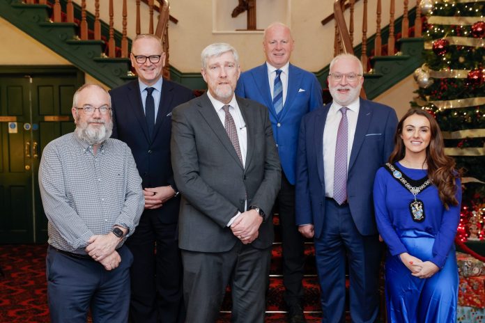 Six people standing on a staircase. One is Lord Mayor, wearing their chain. In the background is a Christmas tree.