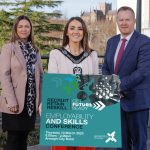 Three people standing together with the person in the middle holding a sign to promote the employability and skills conference.