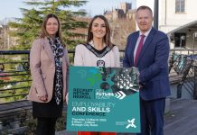 Three people standing together with the person in the middle holding a sign to promote the employability and skills conference.