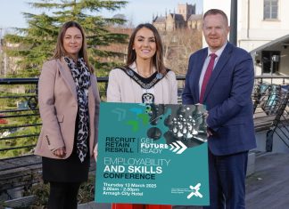 Three people standing together with the person in the middle holding a sign to promote the employability and skills conference.