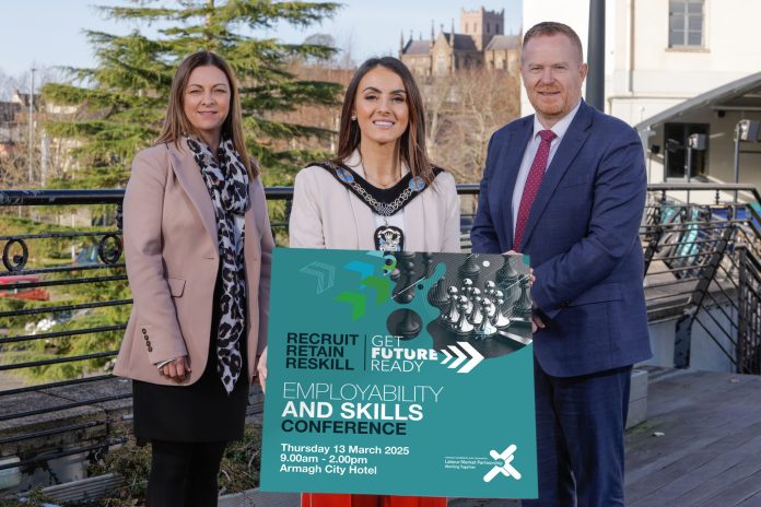 Three people standing together with the person in the middle holding a sign to promote the employability and skills conference.